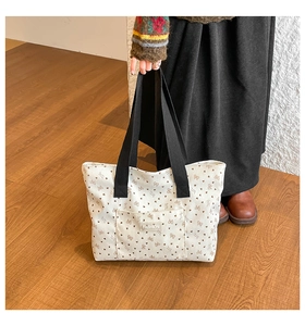 Detail of floral canvas tote bag showing black shoulder straps and fashion logo tag