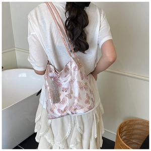 Close-up of pink satin shoulder bag featuring golden butterfly embroidery and grey tassel