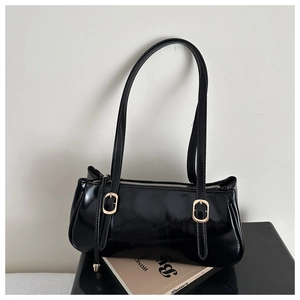 Detail view of black patent leather baguette bag with golden buckles and glossy finish