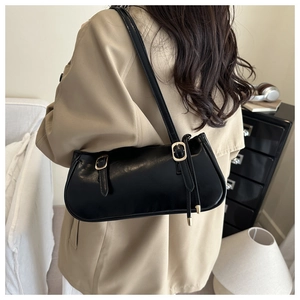 Close-up of black glossy baguette bag with decorative metal buckle straps on shoulder