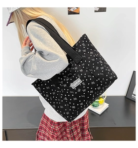 Detail of black tote bag with white heart prints, fashion label and wide strap