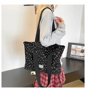 Close-up of black tote bag with white bow and heart prints featuring broad shoulder straps