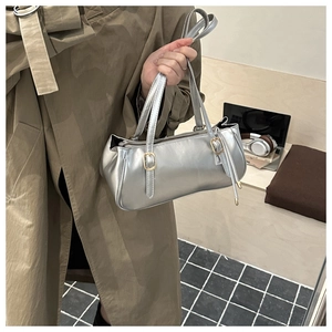 Detail of silver metallic handbag with gold buckles held by a model in a trench coat
