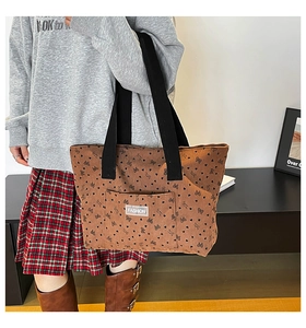 Side view of a brown canvas tote bag with heart patterns worn by a model in casual setting