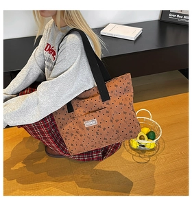 Brown corduroy tote bag with heart bow prints and black shoulder strap shown on a model