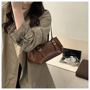 Close-up of caramel leather shoulder bag with golden buckles on a trench coat