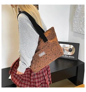 Detail of brown corduroy tote bag with heart and bow patterns worn by a model