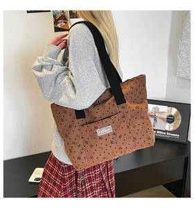 Detail of brown corduroy tote bag featuring black heart and bow prints with a fashion label