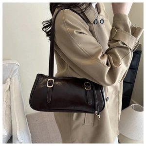 Detail of dark brown baguette bag with gold hardware worn with a classic beige trench coat