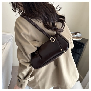 Close-up of a dark brown glossy leather baguette bag worn with a khaki trench coat