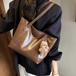 Retro brown leather tote bag with FASHION lettering and bear charm worn by a model