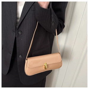 Detail of glossy beige baguette bag with gold lock worn on dark striped blazer