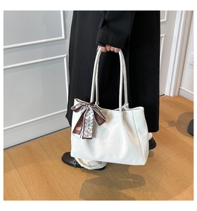 Close-up of white leather tote bag featuring a decorative printed silk scarf on the handle