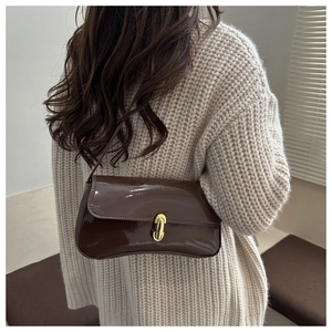 Close-up of glossy dark brown patent leather shoulder bag with gold metal buckle clasp
