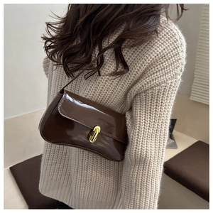 Detail of dark brown patent leather baguette bag with a golden oval metal buckle on a shoulder