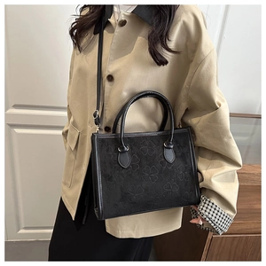 Detail of a black crossbody bag with embossed four-leaf clover patterns and a top handle