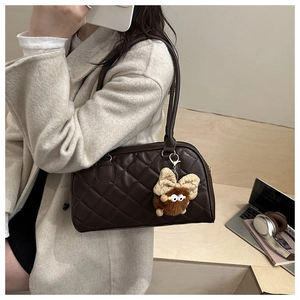 Macro shot of dark brown quilted Boston bag featuring a plush charm on urban wooden steps
