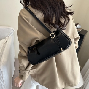 Chic black leather underarm bag with gold hardware worn with a beige trench coat