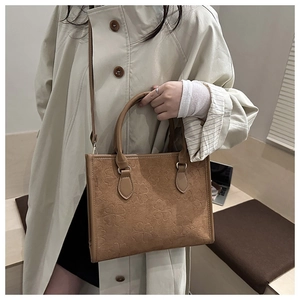 Brown suede crossbody bag with clover embossing worn with a beige trench coat