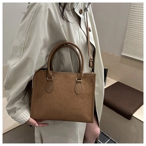 Detail of clover embossed brown suede crossbody bag styled with a beige trench coat