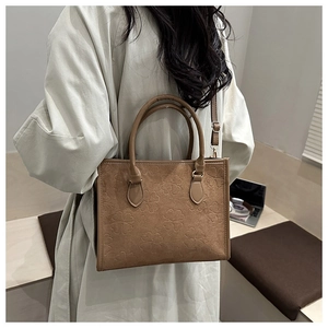 Detail of brown suede tote bag featuring embossed clover patterns and top handles