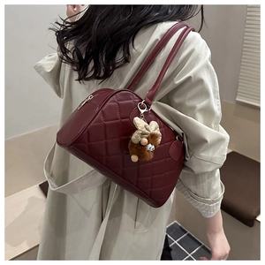 Detail of burgundy quilted shoulder bag with golden zipper and plush charm