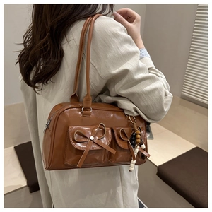 Detail of a brown leather bowling bag with bow pockets and wooden bead charm on a model