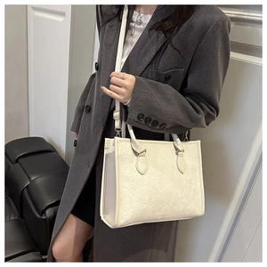 Détail du sac cabas blanc gaufré trèfle porté par un mannequin en blazer gris chic en intérieur