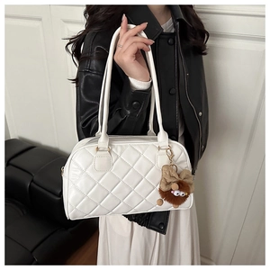 Close-up of white quilted bowling bag with a plush brown pendant for winter 2025 fashion