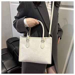 Detail of white tote bag featuring four-leaf clover embossed pattern and metal hardware