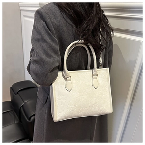 Detail of white tote bag with embossed clover pattern and elegant rolled top handles