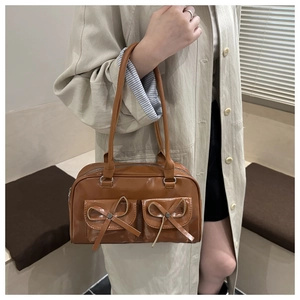 Caramel brown leather shoulder bag with double pockets and bow details on beige trench coat
