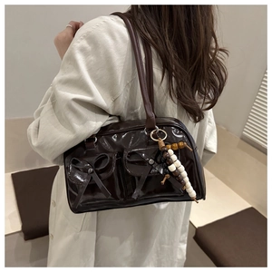 Detail of glossy dark brown patent leather shoulder bag with bow and beaded charm