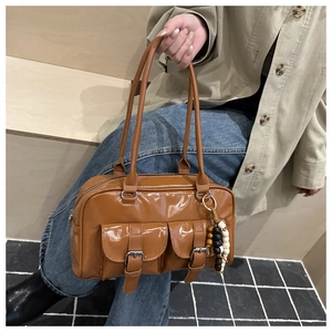 Dettaglio della borsa bowling lucida color caramello con fibbie e ciondolo di perline