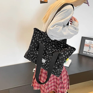 Black corduroy tote bag with white bow and heart prints worn by a model in casual style