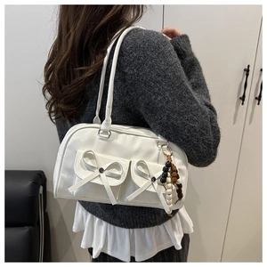 Side view of a white leather bow-decorated bowling bag worn by a model in a grey sweater