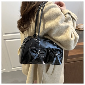 Detail of black patent leather bowling bag with bow pockets shown on a cream coat