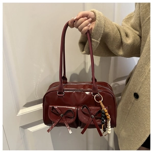 Detail of wine red glossy bowling bag with bow pockets and bead charm held by a model