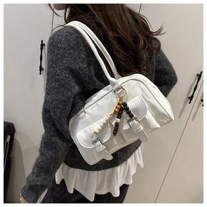 Detail of white leather shoulder bag featuring metal buckles and wooden bead charm