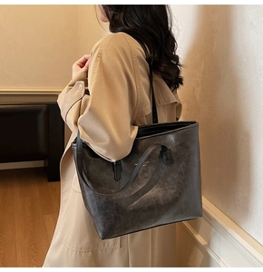 Detail of dark taupe tote bag with vintage texture and golden lettering on shoulder