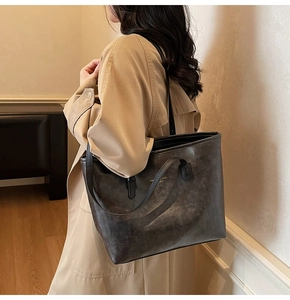Detail of a large dark grey leather tote bag worn by a model in a light camel trench coat