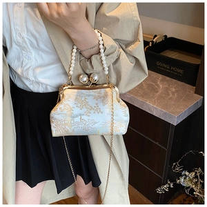 Detail of embroidered silk handbag featuring pearl handle and golden kiss lock closure