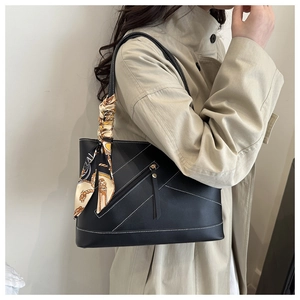 Detail of black leather tote bag featuring white stitching and an elegant printed silk scarf