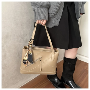 Detail of beige lychee texture tote bag with diagonal zipper and decorative scarf handle