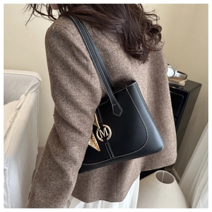 Detail der schwarzen Leder-Tote-Bag mit goldenem M-Logo und Seidenschal am Modell