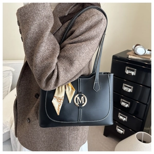 Detail der schwarzen Shopper Tasche mit goldenem M-Logo und Seidenschal-Dekor