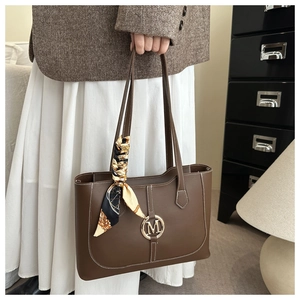 Detail einer braunen Shopper-Tasche mit goldenem M-Logo und dekorativem Seidenschal