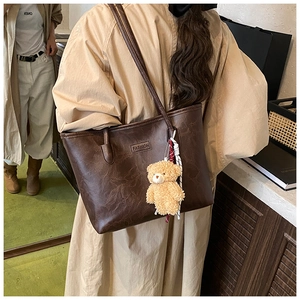 Detail of dark brown faux leather tote bag with FASHION label and plush bear charm