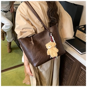 Detail of dark brown leather tote bag with fashion label and cute teddy bear charm