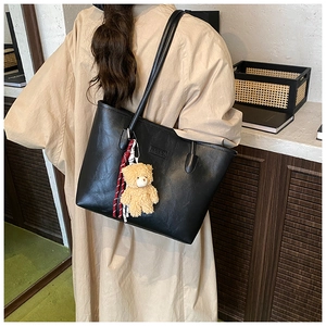 Detail of black tote bag with Fashion embossing and a cute brown bear charm